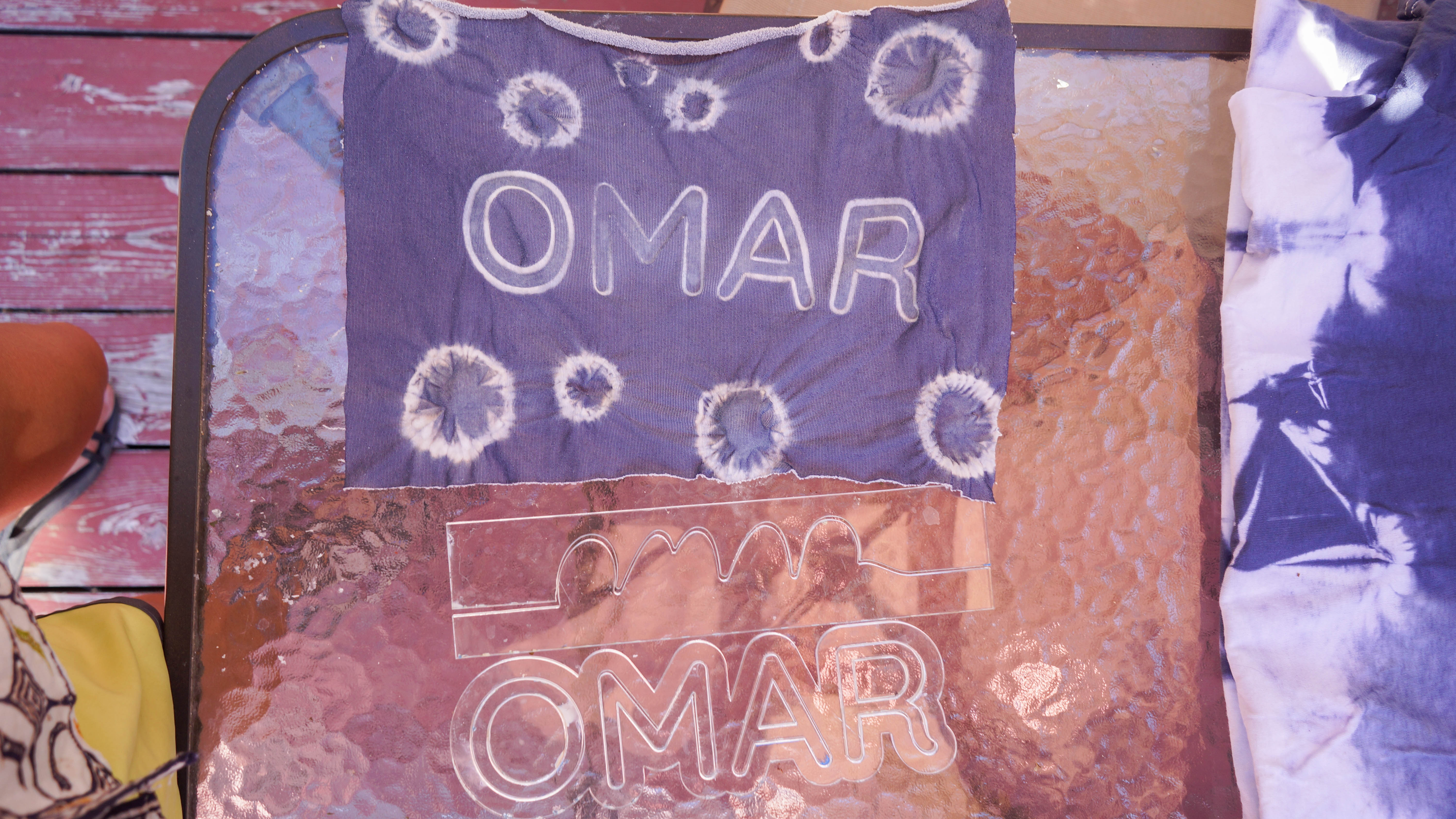 Shibori fabric spelling out 'OMAR', with laser cut resists used for dyeing below the fabric